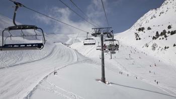 A ski lift carries a group up along a mountainside, allowing them to enjoy the surrounding views of vast snowy slopes and clear blue skies.