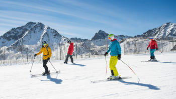 A group of skiers glide their way down a slope, surrounded by panoramic views of snowy mountains.
