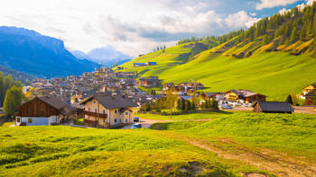 San Cassiano in Alta Badia nestles peacefully in a green alpine valley, framed by the towering, jagged peaks of the Dolomites and dotted with traditional wooden chalets.