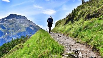 Hiker walking up a scenic trail in the Neustift mountains, surrounded by rocky peaks and alpine meadows under a blue sky