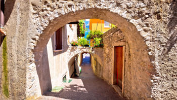 Scenic view through a stone archway in the old town of Limone, revealing narrow cobbled streets and historic buildings bathed in warm sunlight.