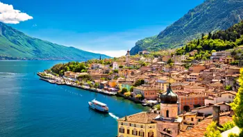 View of Limone sul Garda in Italy with a colourful boat floating on the calm waters of Lake Garda, backed by charming lakeside houses and steep cliffs.