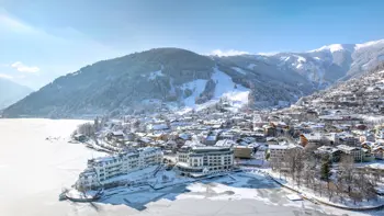 A drone shot of the Hotel and it's surroundings from above, showing its place amongst vast snowy mountains under clear blue skies.