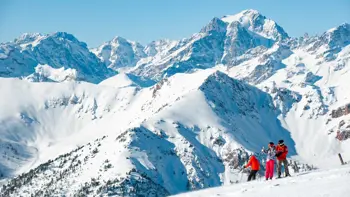 Montgenèvre offers stunning mountain views, with rolling snow-covered slopes and rugged alpine peaks stretching into the distance, framed by clear blue skies and dotted with larch trees