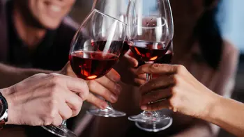 A collection of glasses holding red wine tap together as a group signals a toast.