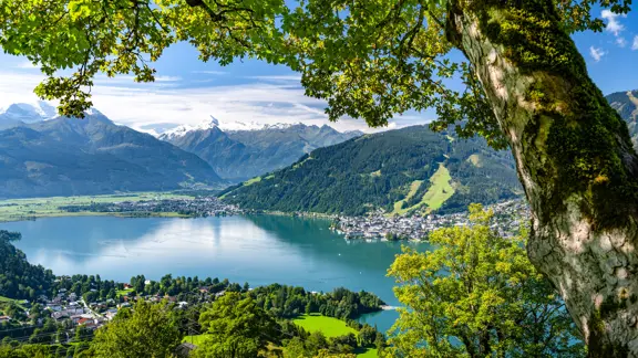 Tranquil view of Lake Zell surrounded by mountains, with reflections on the water and the town of Zell am See along the shoreline.