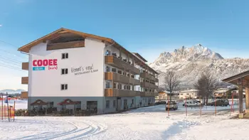 A look at the hotel's exterior in a snow covered landscape, with mountains and clear blue skies behind.