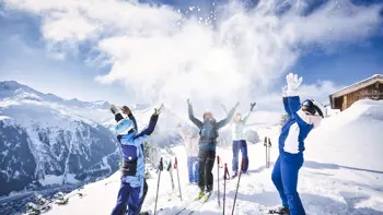 A group of skiers celebrate and relax atop a mountain range in St. Anton, surrounded by panoramic views of the snow covered peaks.