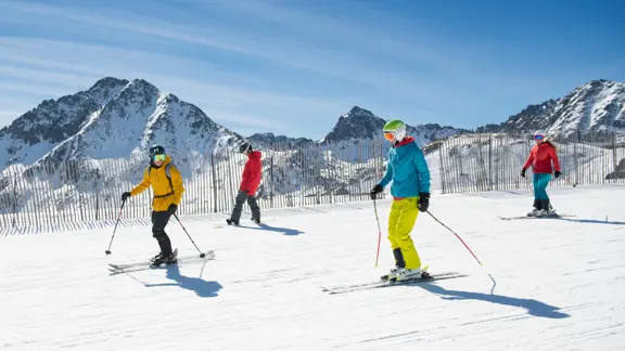A group of skiers glide their way down a slope, surrounded by panoramic views of snowy mountains.