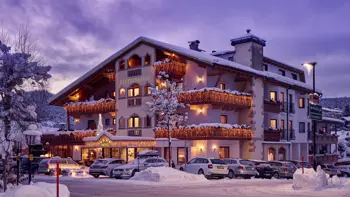 A shot of the hotel's exterior, with warm light shining from the windows and snowy mountains in the background.