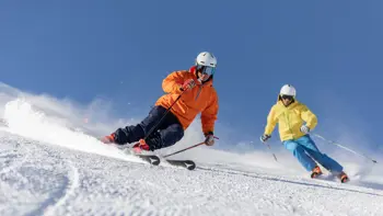 Two skiers gliding down a snowy slope in Livigno under a clear blue sky.