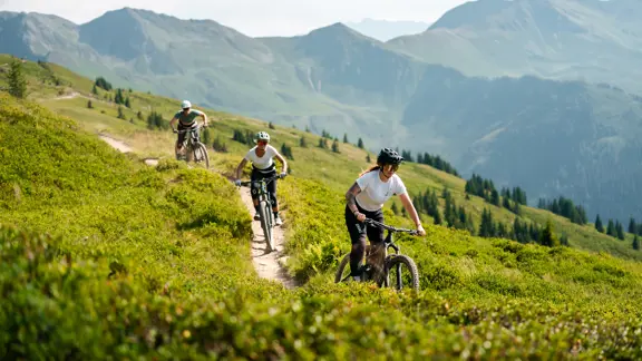 Group of cyclists riding together through the scenic Saalbach Hinterglemm mountains, surrounded by lush greenery and rugged peaks.