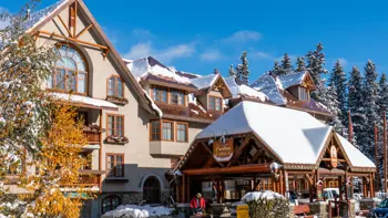 The exterior of Banff Caribou Lodge & Spa in winter presents a charming alpine retreat, with its hand-hewn log architecture, snow-covered rooftops, and a welcoming entrance