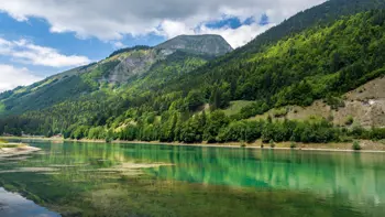 Peaceful view of Lac de Montriond near Morzine, with calm turquoise water surrounded by dense forest and steep mountain slopes.