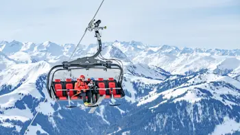 A group of skiers climb a ski lift, taking in the surrounding mountains and clear skies.