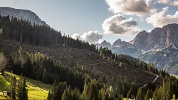 Colfosco in Alta Badia sits nestled beneath the dramatic Dolomite peaks, with its quaint alpine buildings surrounded by lush green meadows and rugged mountain scenery.