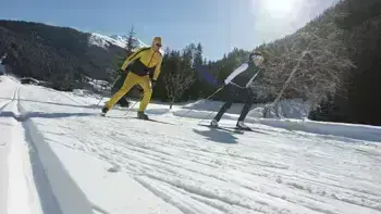 Two skiers swiftly descend a mountain slope, carving through fresh powdered snow.