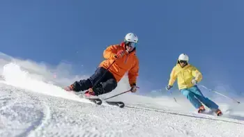 Two skiers gliding down a snowy slope in Livigno under a clear blue sky.