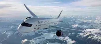 Air Canada airplane flying high in the sky above snow-covered mountains on a clear day.