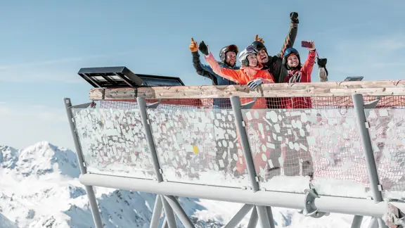 A group of skiers take a selfie atop a viewing platform, looking across the vast mountains and valleys of Solden, Austria.