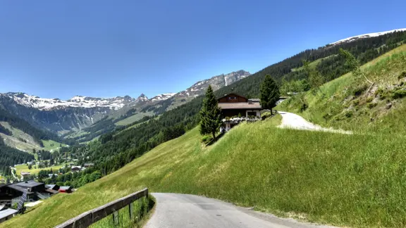 Small wooden chalet on a grassy hillside under a clear blue sky in Saalbach Hinterglemm.