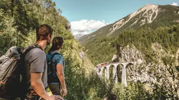 A couple looking out to the Switzerland Landwasser Viaduct, surrounded by lush forests and giant mountains.