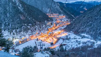 An aerial shot of Arinsal ski resort, with warm orange light glowing from the buildings tucked into vast snowy mountains.