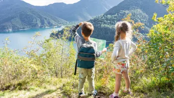 Young children standing on a hillside, looking out over the sparkling waters of Lake Ledro surrounded by green mountains.