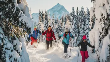 A family snoeshoeing together in the Cortina forests, surrounded by snow under a clear sky.