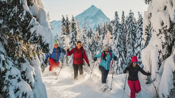 A family snoeshoeing together in the Cortina forests, surrounded by snow under a clear sky.