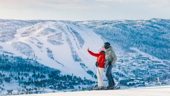 A couple taking a selfie atop of a snowy mountain in Geilo, surrounded by peaks and lush winter forests.