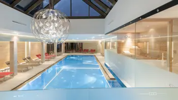 A view of a clear indoor swimming pool from within the Hotel, with bright blue sky seen from the windows above.