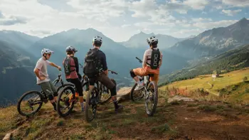 Group of cyclists standing at the summit of an Obergurgl mountain, looking out over a panoramic view of alpine peaks and valleys