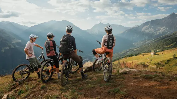 Group of cyclists standing at the summit of an Obergurgl mountain, looking out over a panoramic view of alpine peaks and valleys