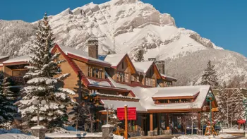 The exterior of the Banff Ptarmigan Inn is a three-story, classic post-and-beam mountain lodge featuring natural wood accents, large windows, and a welcoming entrance, situated just steps from downtown Banff along Banff Avenue.