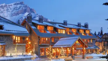 The Fox Hotel & Suites in Banff features a warm, alpine-style exterior with timber and stone accents, nestled in a snowy winter setting along Banff Avenue.