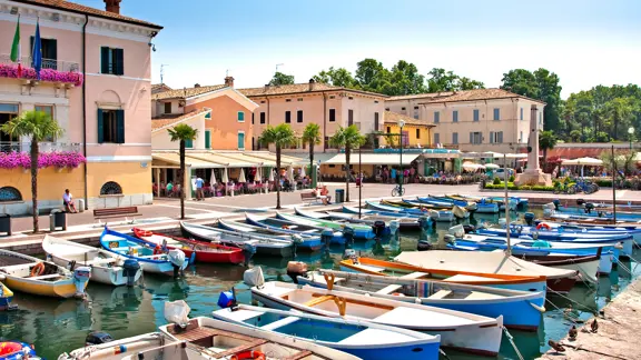 Small boat dock in Bardolino, with moored boats gently floating on the clear waters of Lake Garda, framed by a peaceful lakeside setting.